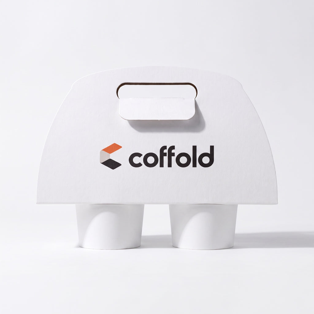 Coffold two-cup drinks carrier in white board, locking tab folded through the handle slot, holding two takeaway coffee cups